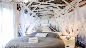 Een rond bed met een grijze matras en kussens, een hanglamp erboven en een houten vloer.