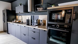 Een moderne keuken met grijze kastjes, een zwarte koelkast, een inbouwoven en een magnetron.