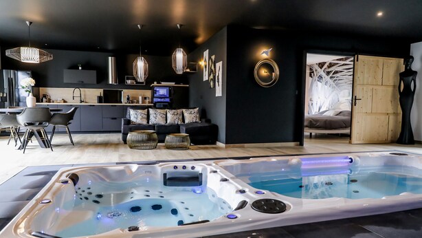 Een moderne spa met een groot bubbelbad, een gezellige zithoek met een bank en stoelen, en een kitchenette met een televisie.