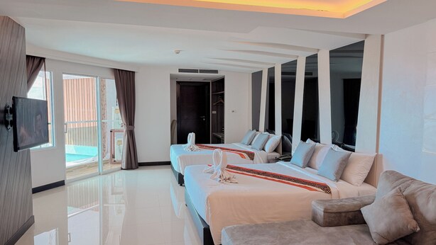 A modern hotel room with two beds, a sofa, a TV, and a balcony with a view. - Vareena Palace Hotel (Pattaya)
