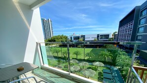 A balcony with a view of a landscaped area, including palm trees and a pool, and modern buildings in the background. - Vareena Palace Hotel (Pattaya)