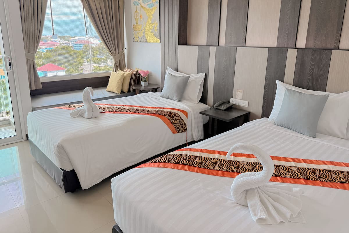 Ein Hotelzimmer mit zwei Betten, einem Fenster mit Vorhängen, einem kleinen Tisch mit Telefon und einem Wanddekor.