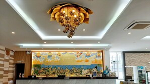 A hotel reception area with a large mural, a chandelier, and a reception desk. - Vareena Palace Hotel (Pattaya)