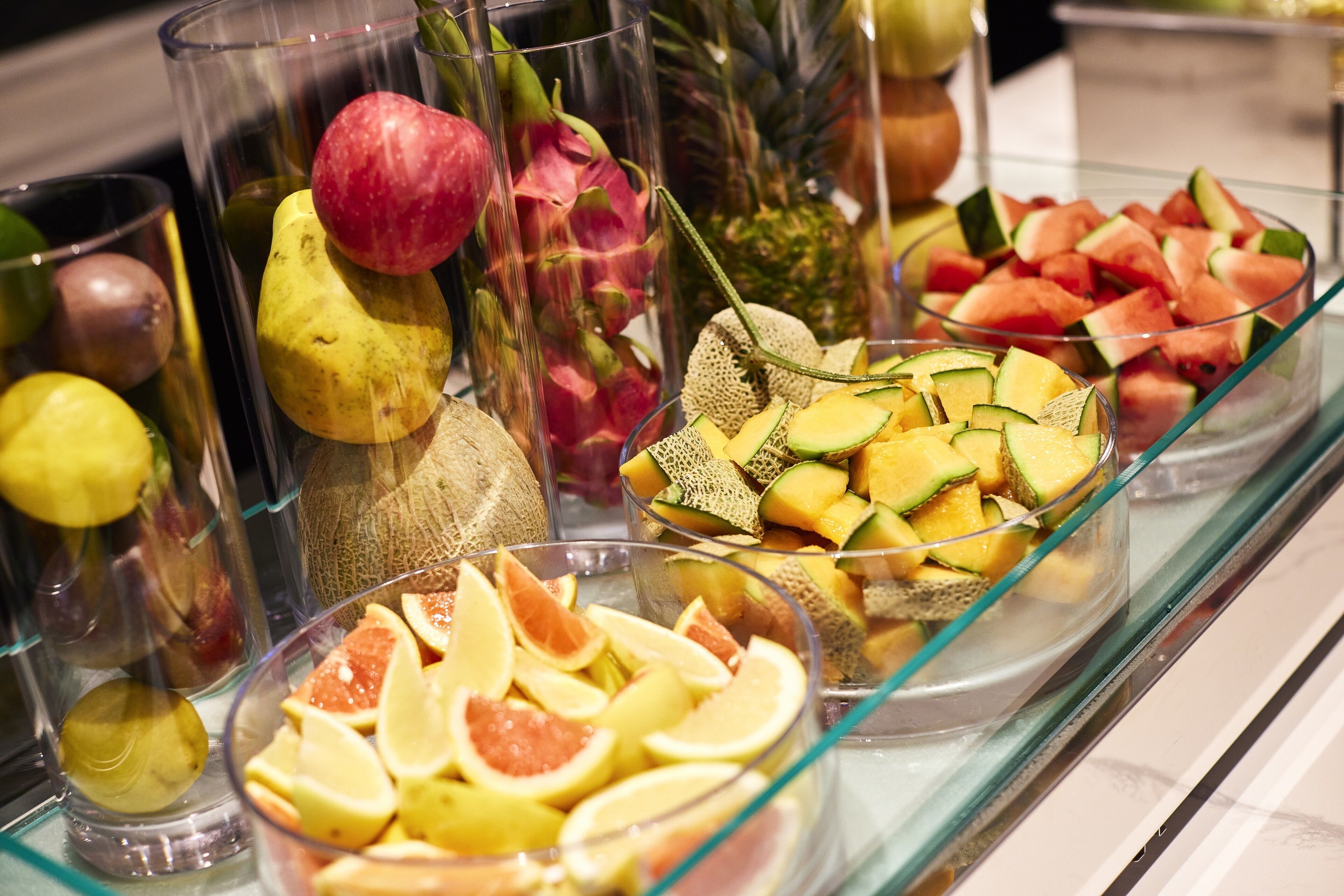 Un bufé con frutas y verduras de diversos tipos, exhibidas en recipientes de vidrio transparente.
