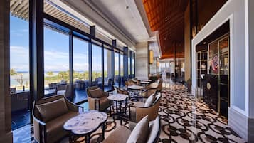 A spacious indoor area with large windows overlooking a beach, furnished with multiple seating arrangements and a patterned floor.