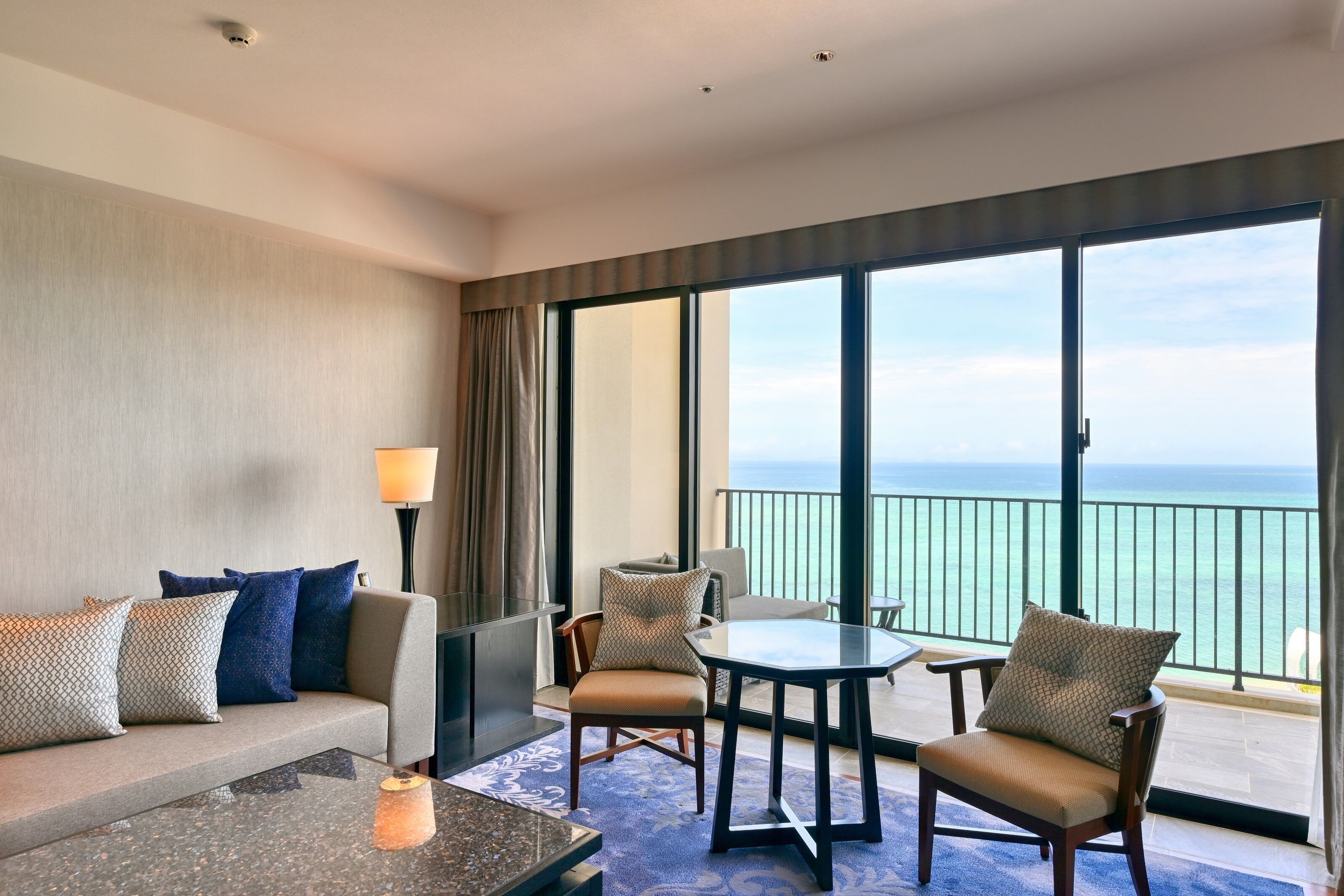 A hotel room with a balcony, a sofa, a table, and chairs.