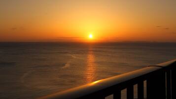 A sunset over the ocean with a railing in the foreground.