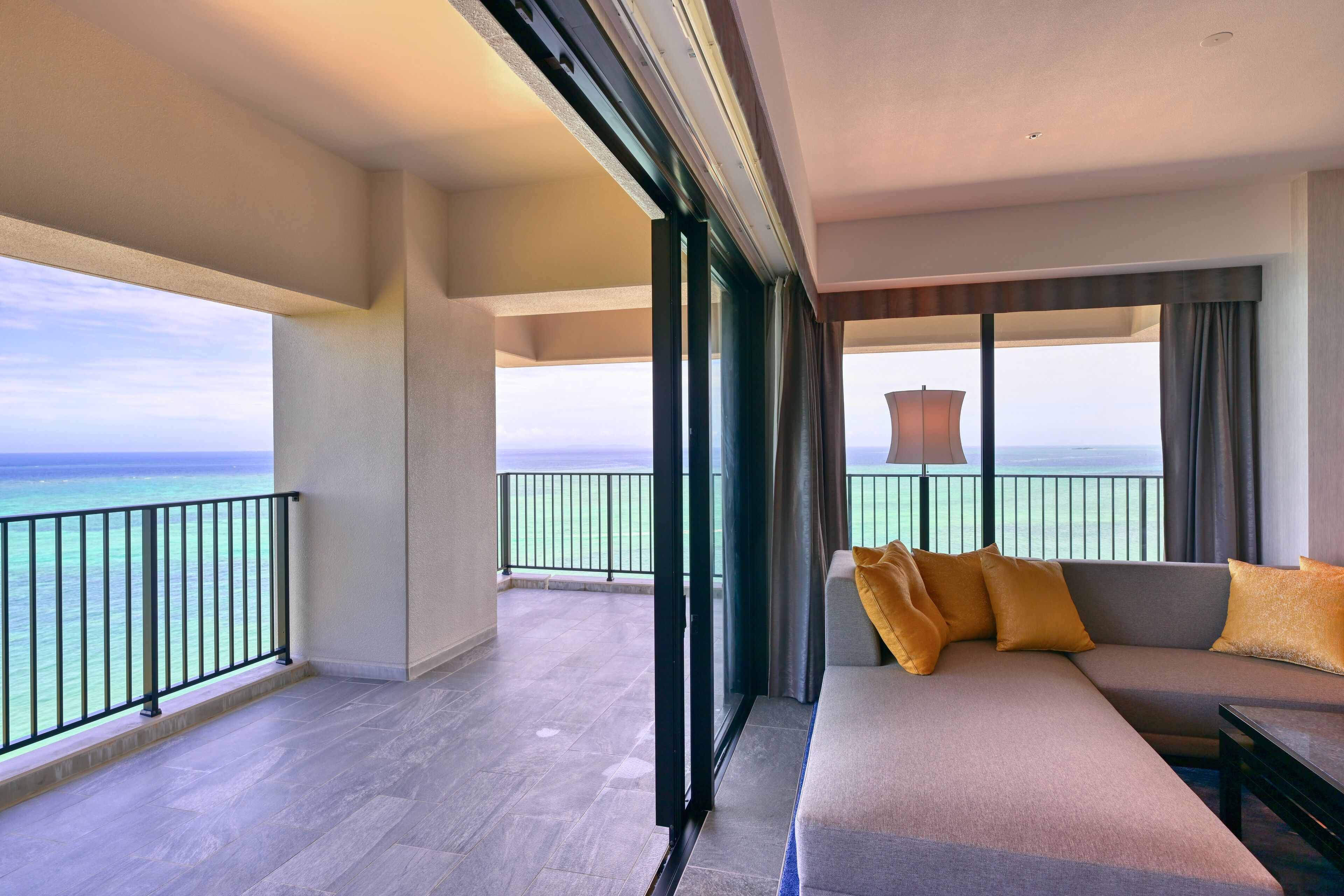 A modern hotel room with a balcony, a sofa with cushions, and a view of the ocean.