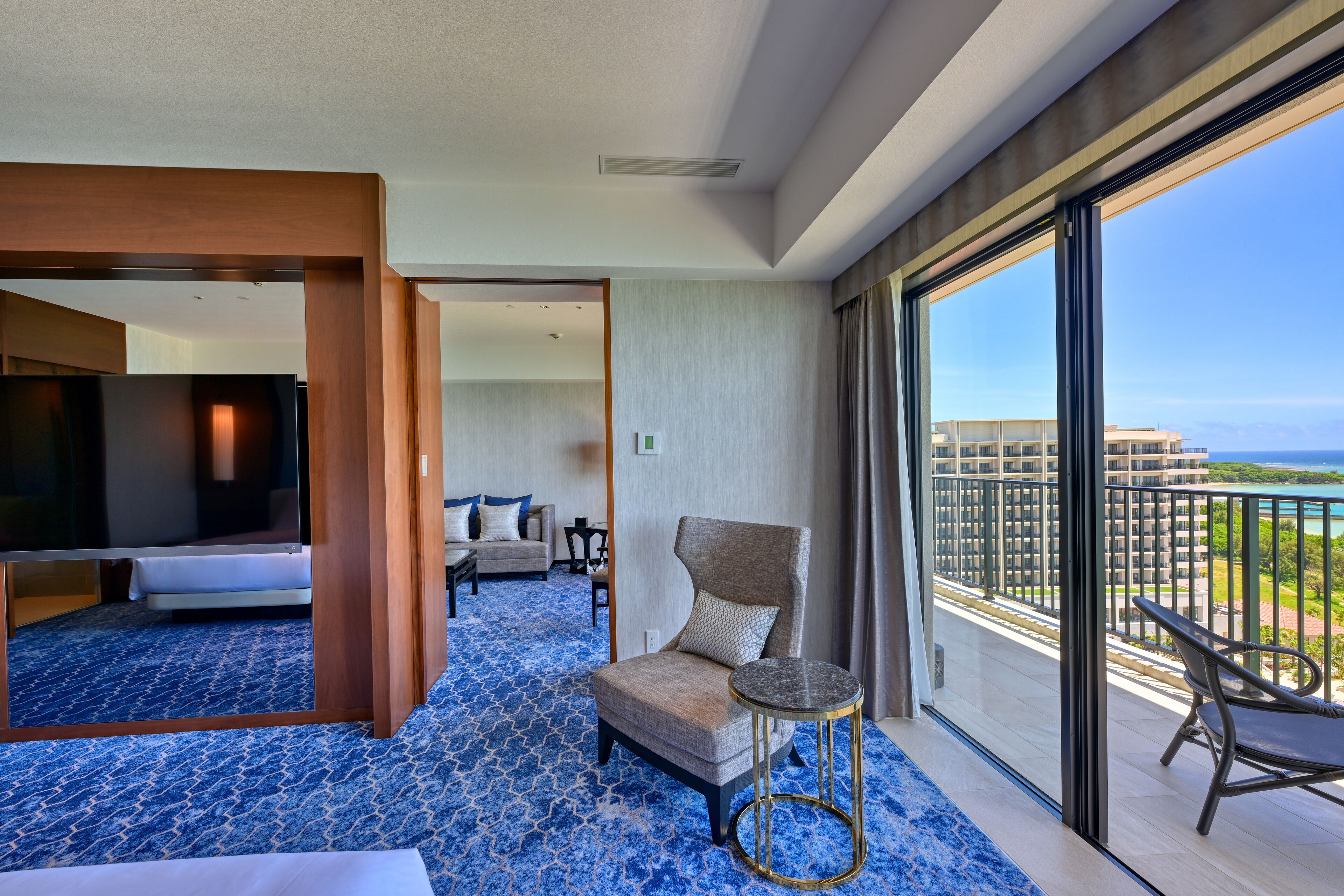 A hotel room with a large balcony, a bed, a chair, and a small table.