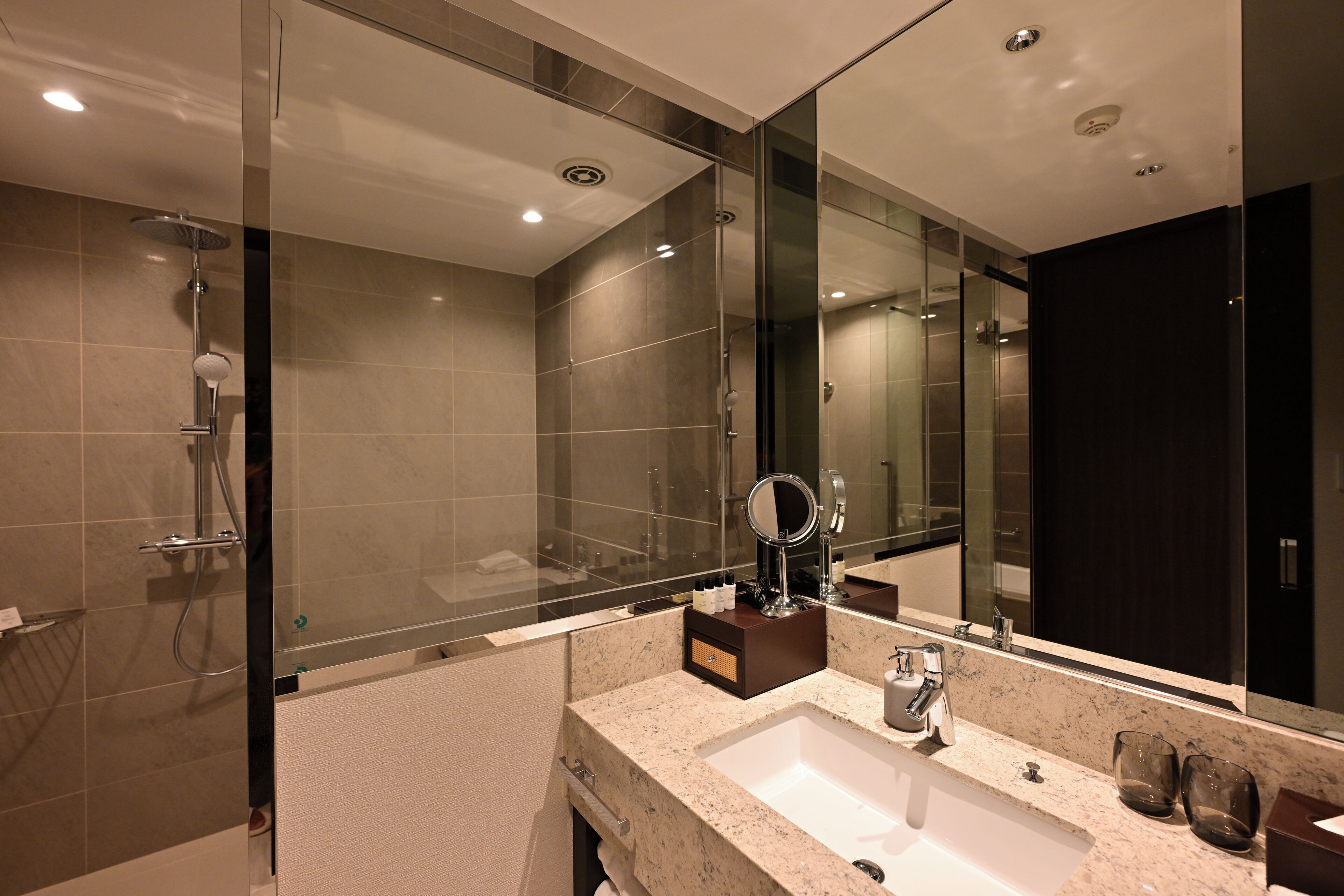 A modern bathroom with a glass-enclosed shower, a large mirror, and a marble sink.