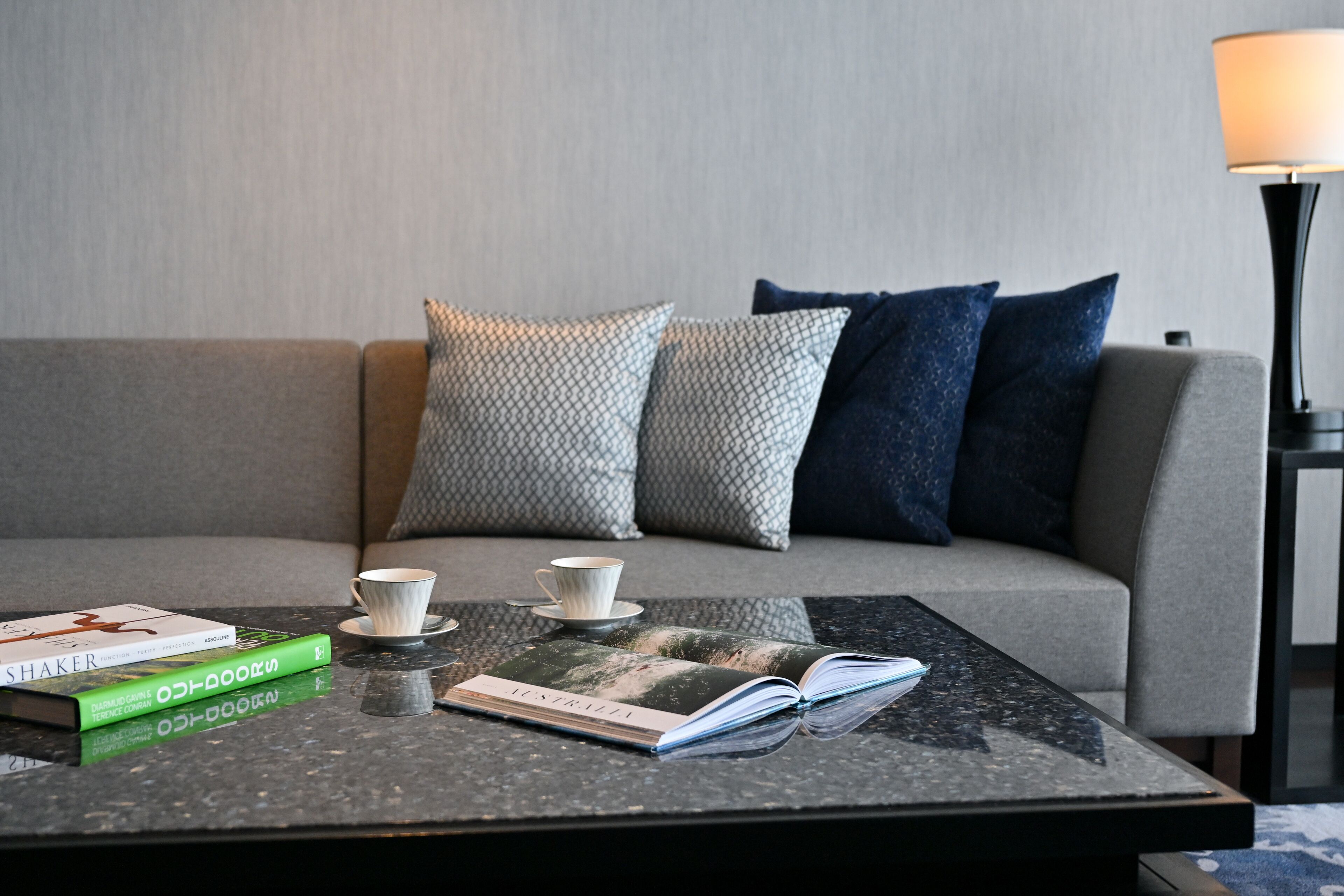 A modern living room with a grey sofa, patterned cushions, a coffee table with books and a cup, and a floor lamp.