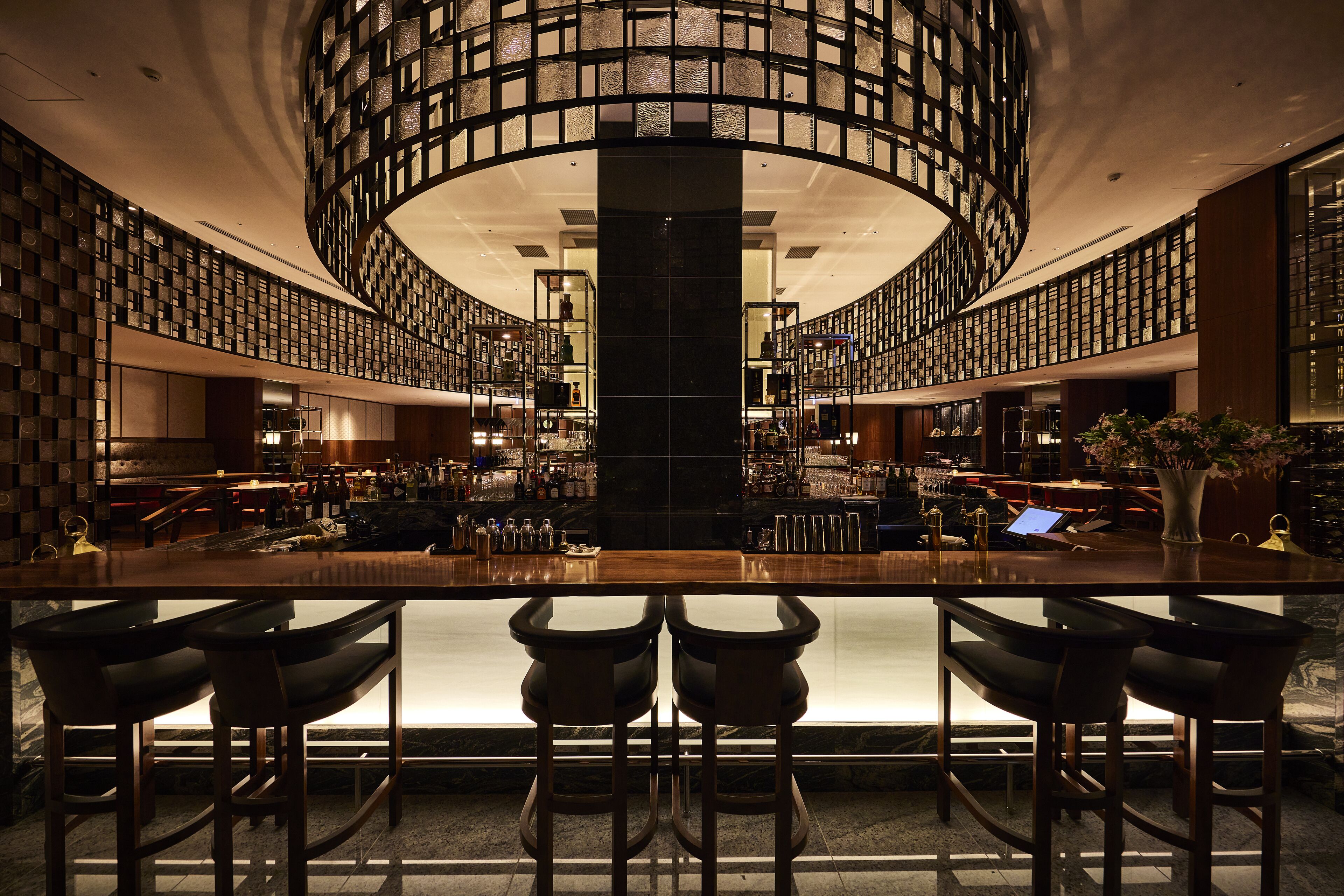 A bar area with a central column, multiple bar stools, and a circular ceiling design.