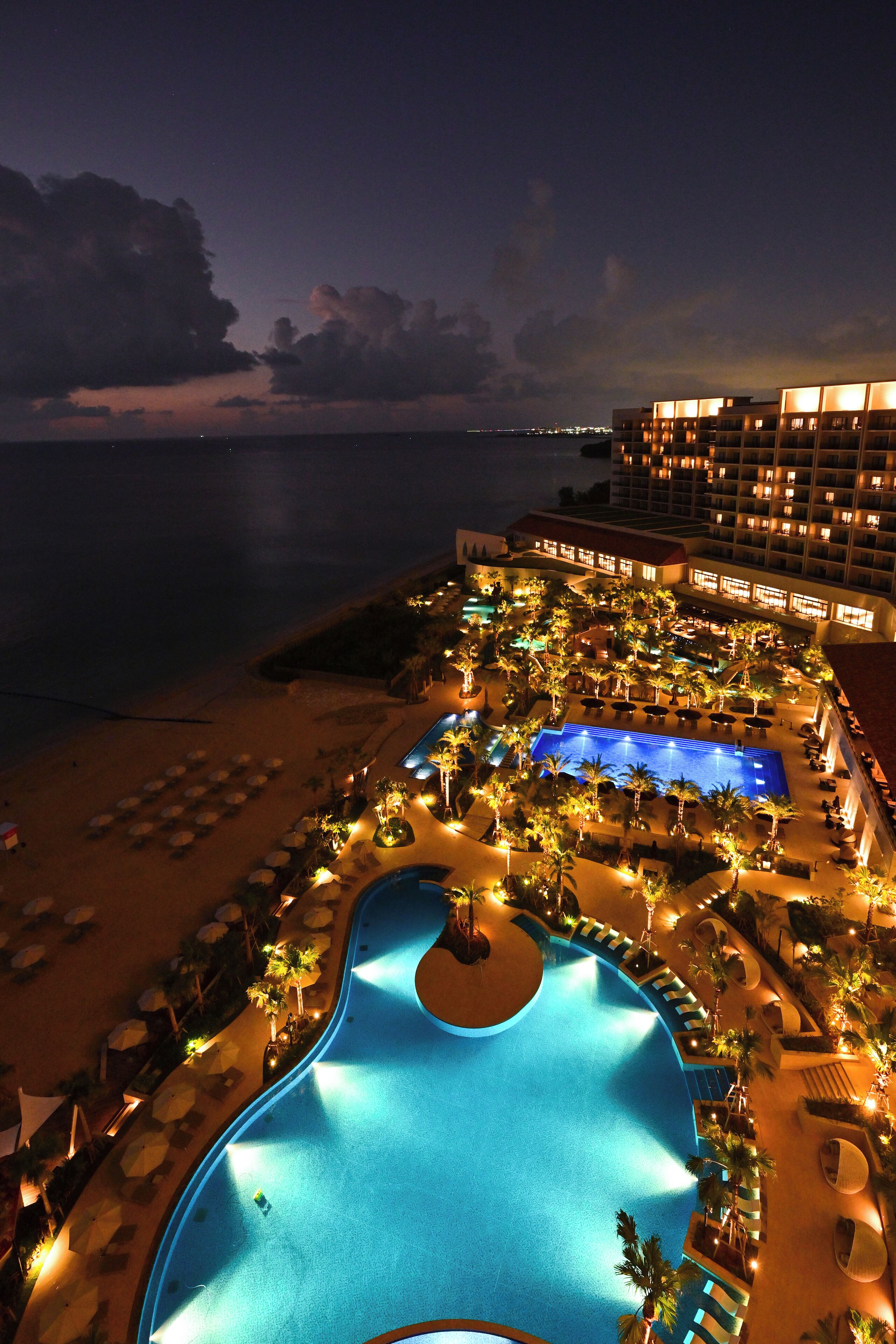 A resort with a large swimming pool, palm trees, and beachfront views.