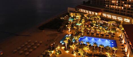A resort with a large swimming pool, palm trees, and beachfront views.
