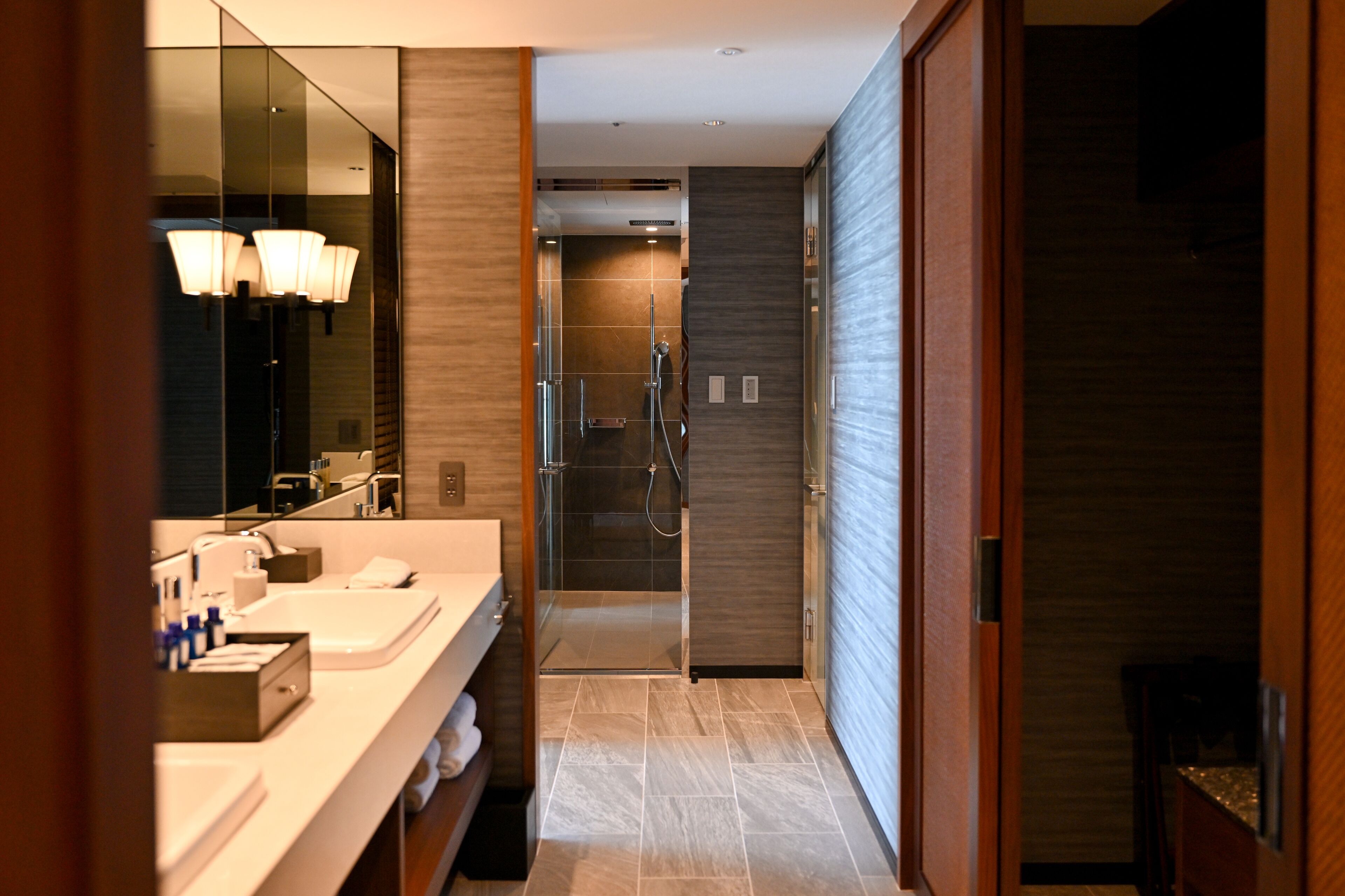 A modern bathroom with a walk-in shower, a large mirror, and a vanity with multiple sinks and toiletries.