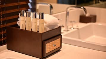 Un baño con una caja de madera que contiene artículos de aseo, un lavamanos blanco y un espejo.