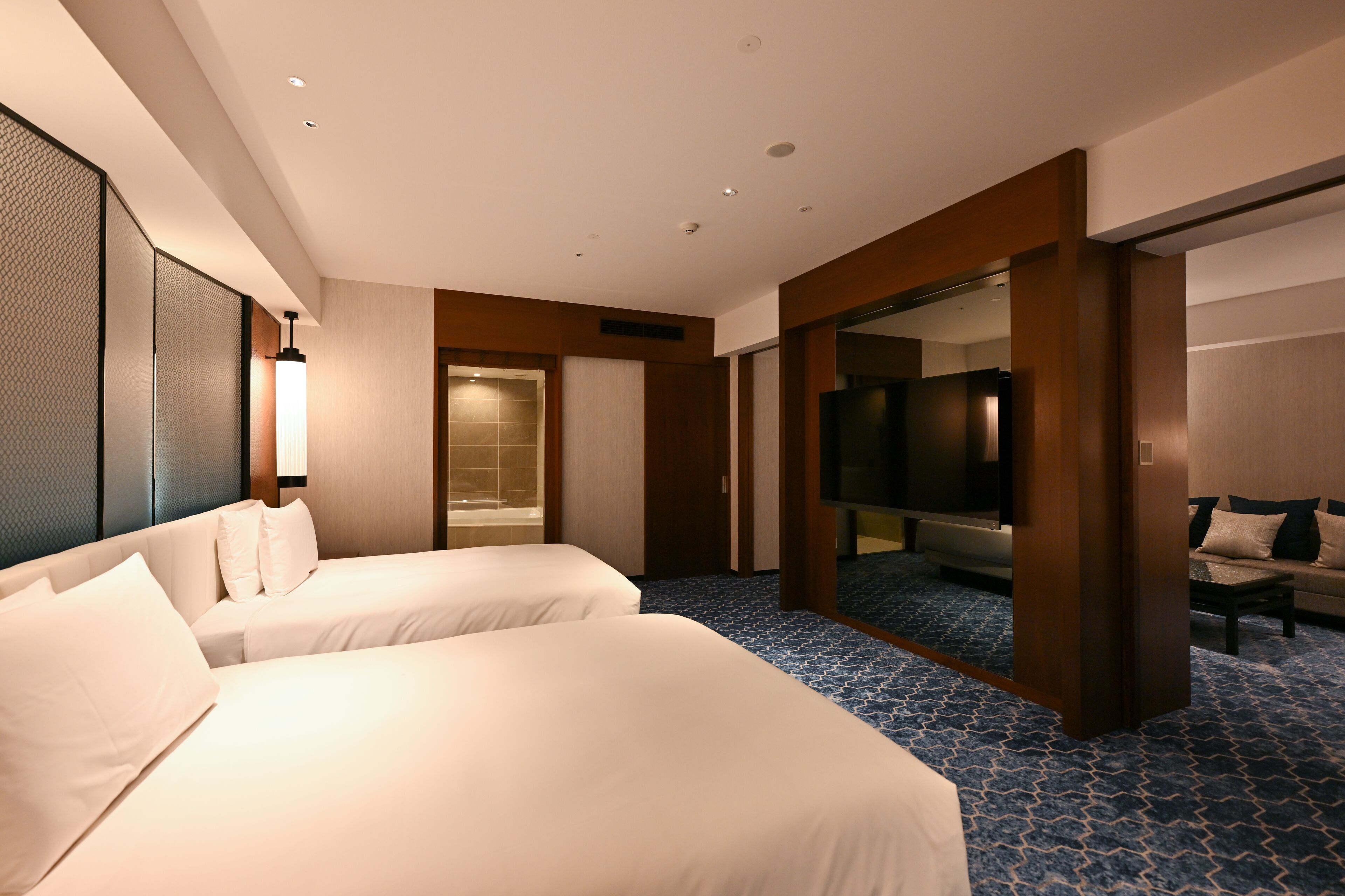 A hotel room with two beds, a large mirror, a TV, and a bathroom with a bathtub.
