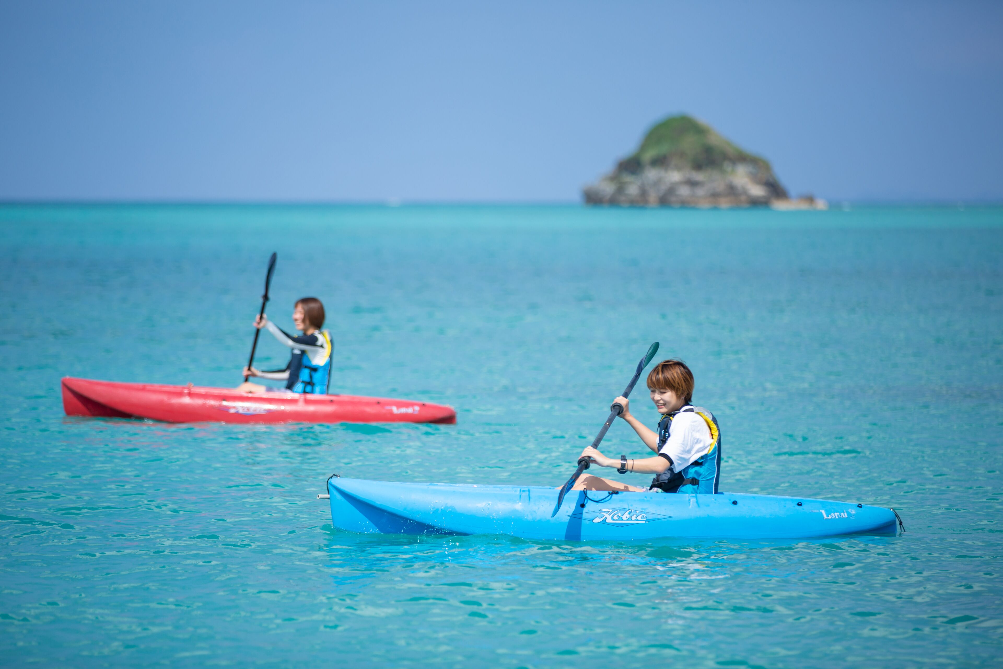 Two kayaks on calm water with a clear view of the sea and a small island in the distance.