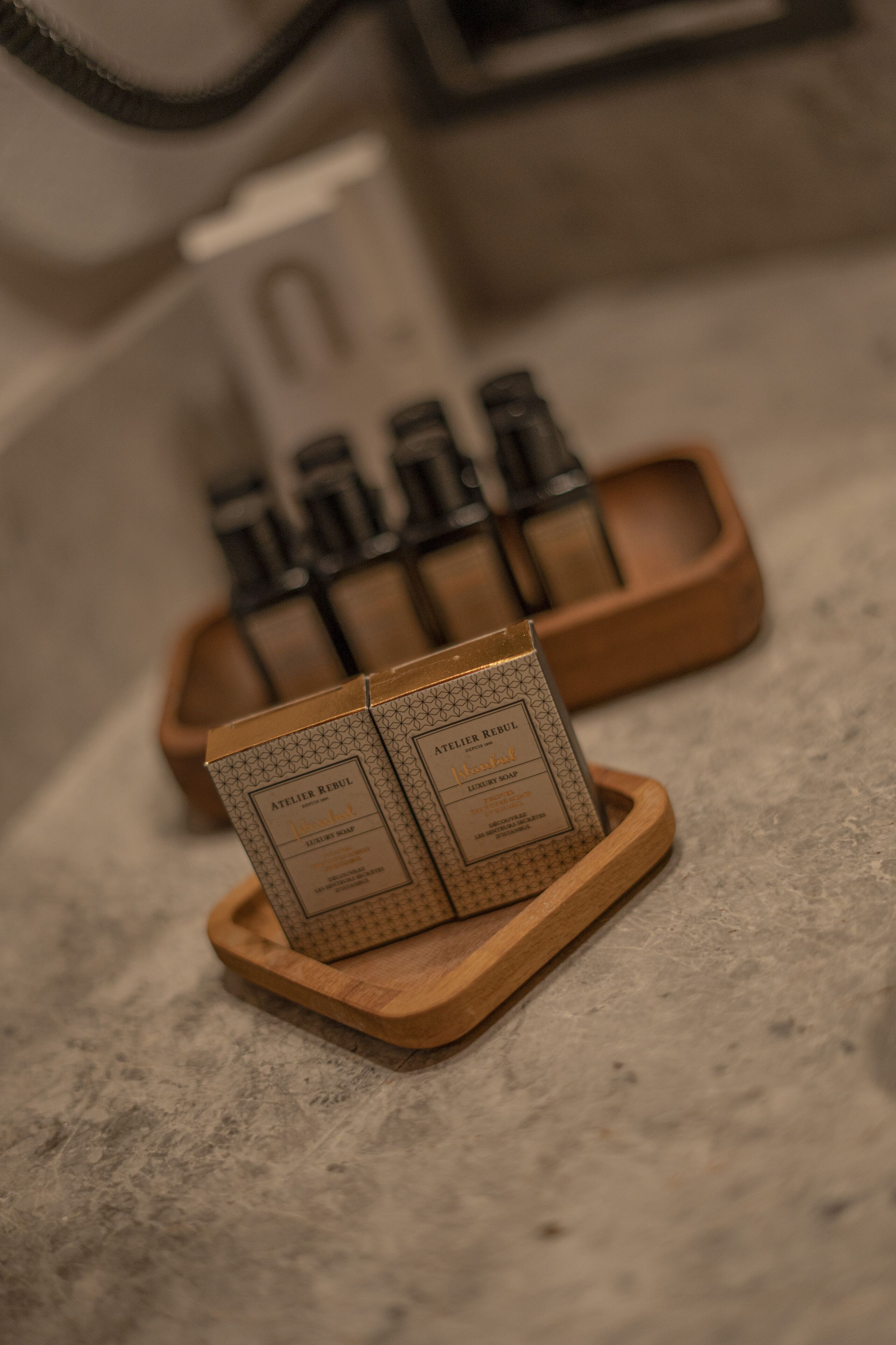 A wooden tray holding two boxes labeled "Atelier Rebul" on a textured surface.