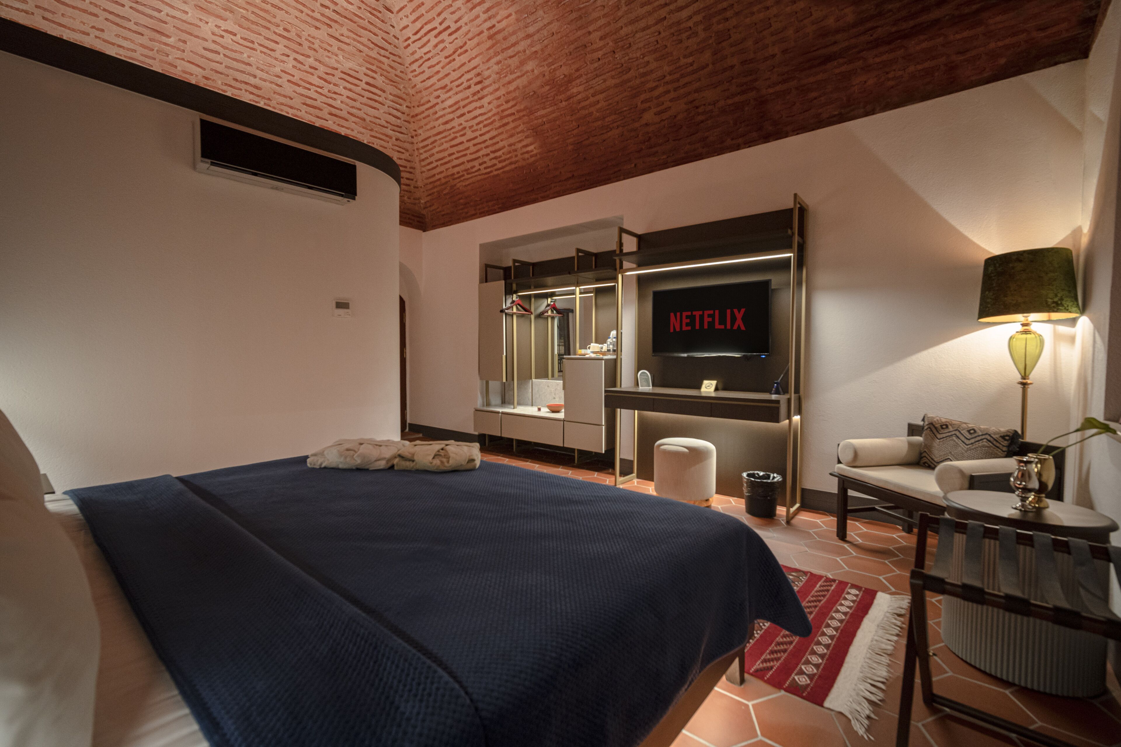 A hotel room with a bed, a desk with a computer, a TV, and a lamp.