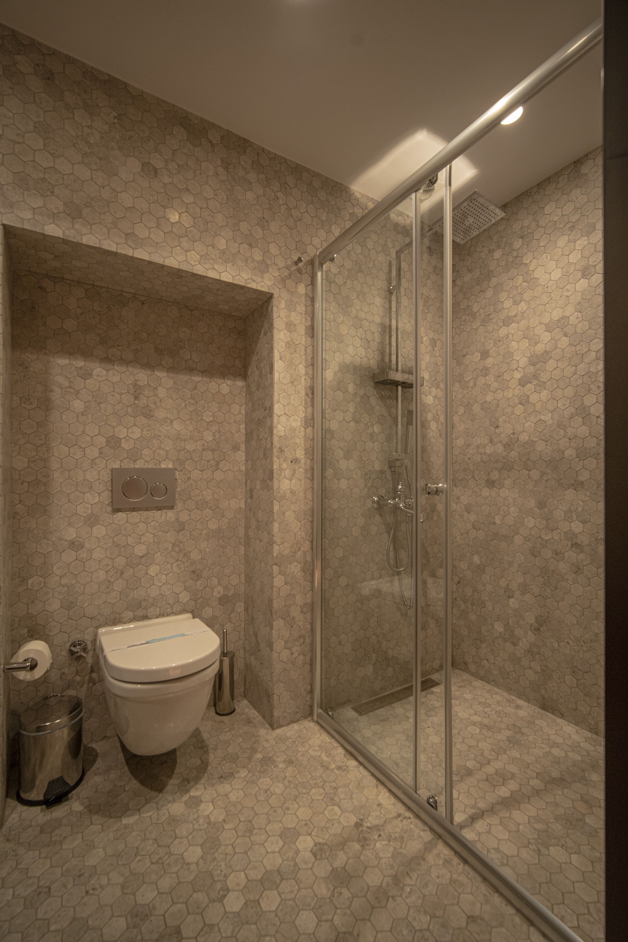 A modern bathroom with a glass-enclosed shower, a toilet, and a trash can.