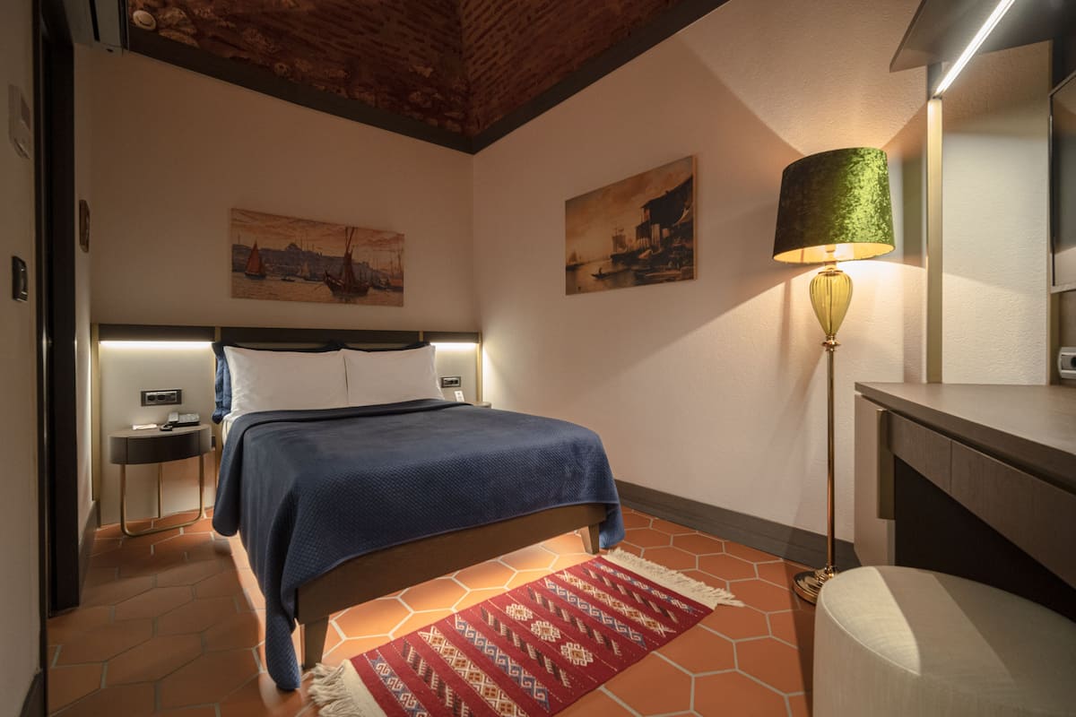 A bedroom with a bed, a nightstand, a lamp, and two paintings on the wall.