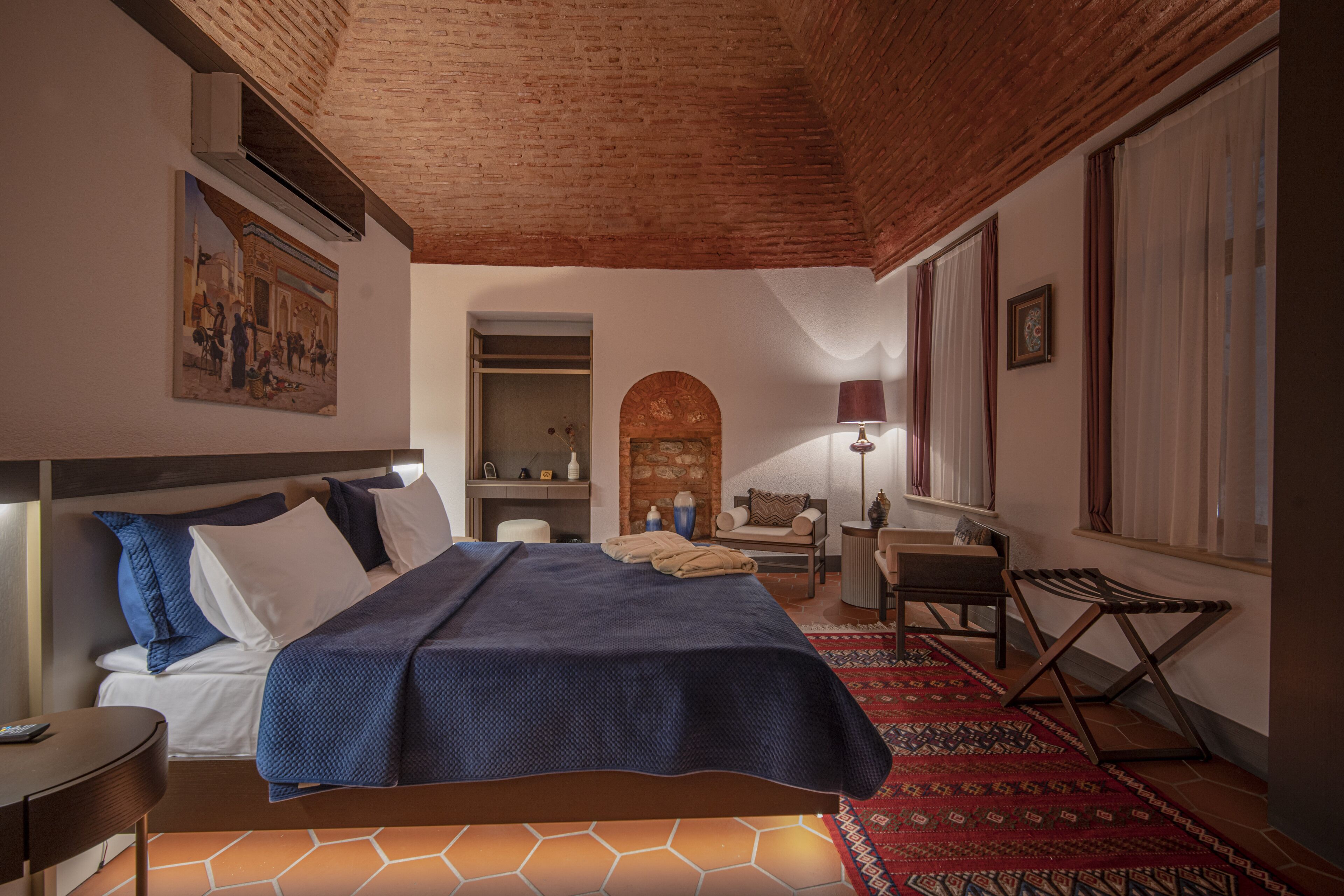 A hotel room with a bed, a desk, a chair, a lamp, and a window with curtains.