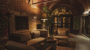 Un rincón salón acogedor, con luz tenue, una pared de ladrillo rústico, un conjunto de sofás, una mesa de centro y una lámpara de pie grande.