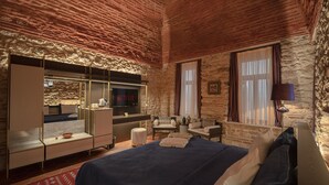 Un dormitorio con una cama grande, televisión, escritorio y pared de piedra.