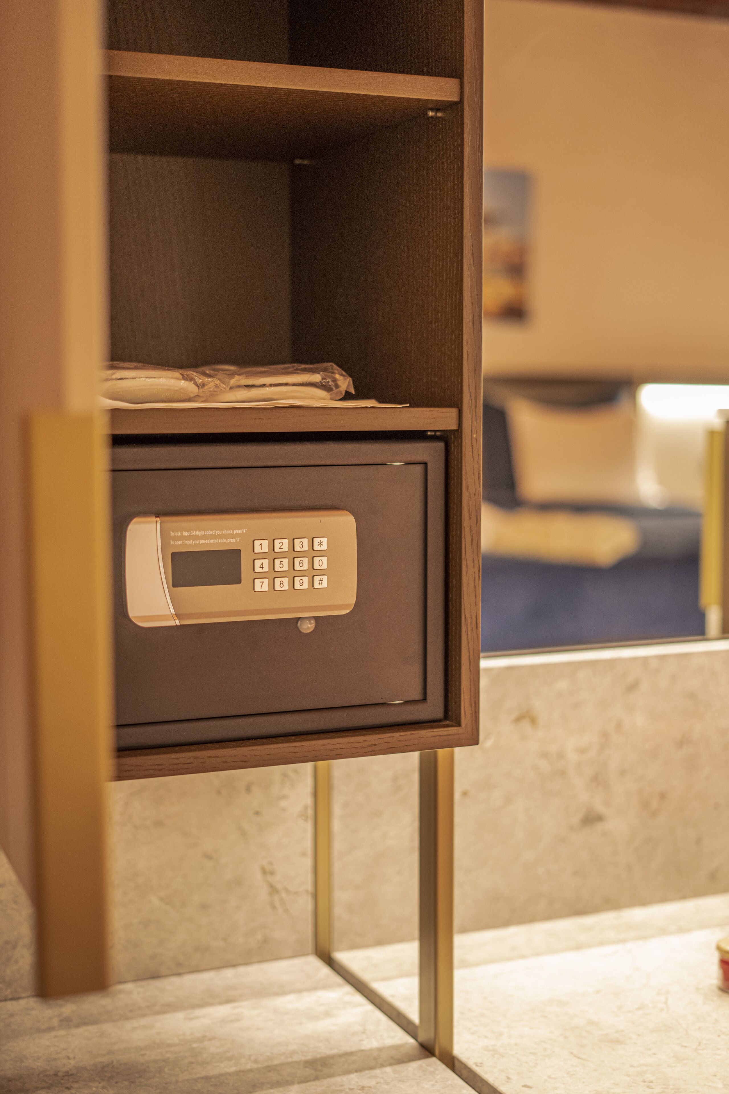 Een hotelkluis met een keypad, een bed met een blauwe spreidek en een raam met uitzicht op de kamer.