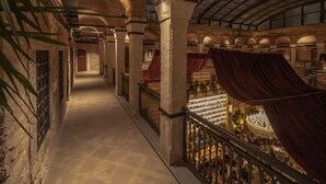 Un salón imponente con techos altos, columnas abovedadas y una escalera que baja a un nivel inferior.