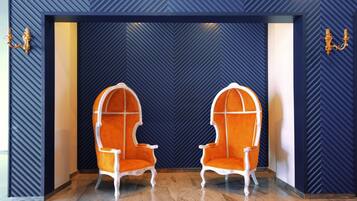 Two ornate chairs with white frames and orange upholstery, positioned in front of a wall with a chevron pattern.