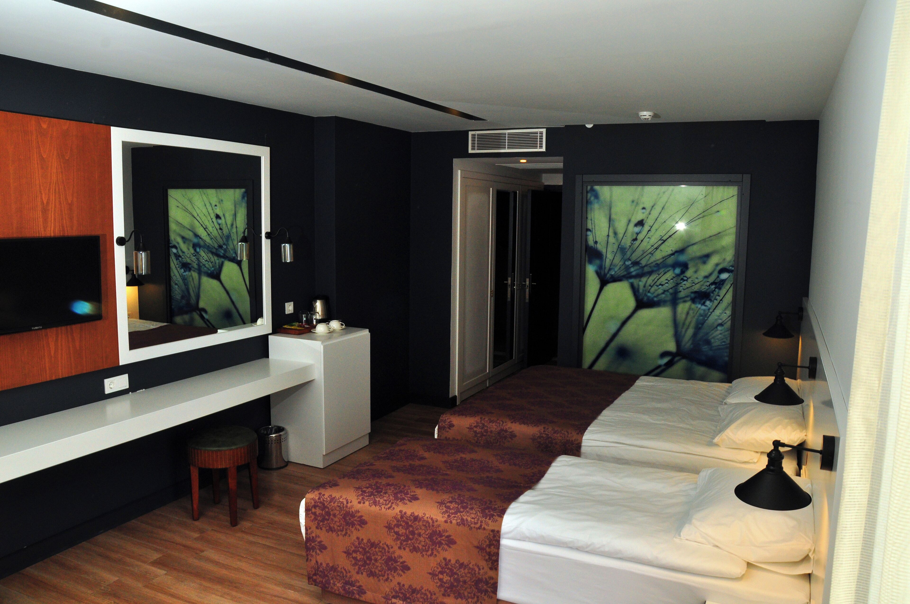 Habitación de hotel con un espejo grande, un escritorio, una silla, dos camas y una lámpara fijada a la pared.
