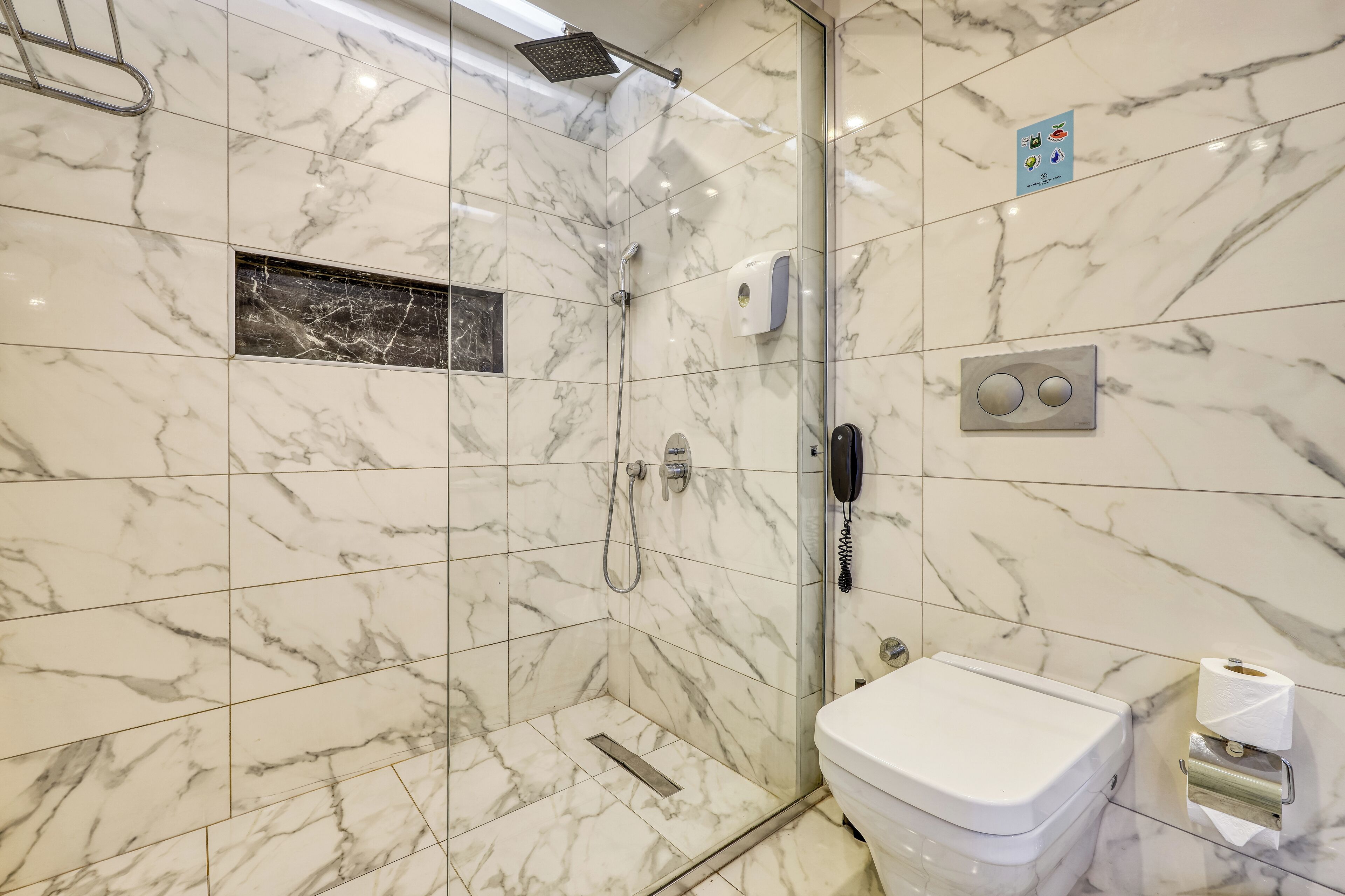 A bathroom with marble tiles, a shower, a toilet, and a hand dryer.
