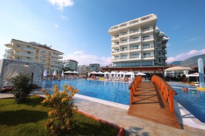 A swimming pool with a wooden deck, surrounded by buildings and umbrellas. - SEY BEACH HOTEL &SPA (Alanya)