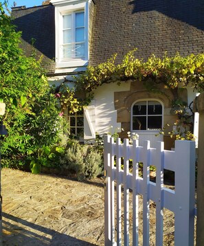 Une maison avec une clôture en bois peinte en blanc, une façade en pierre et une fenêtre à cadre blanc.