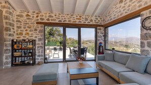 Un salon spacieux aux murs en pierre, doté d’une grande fenêtre et offrant une vue sur l’extérieur.