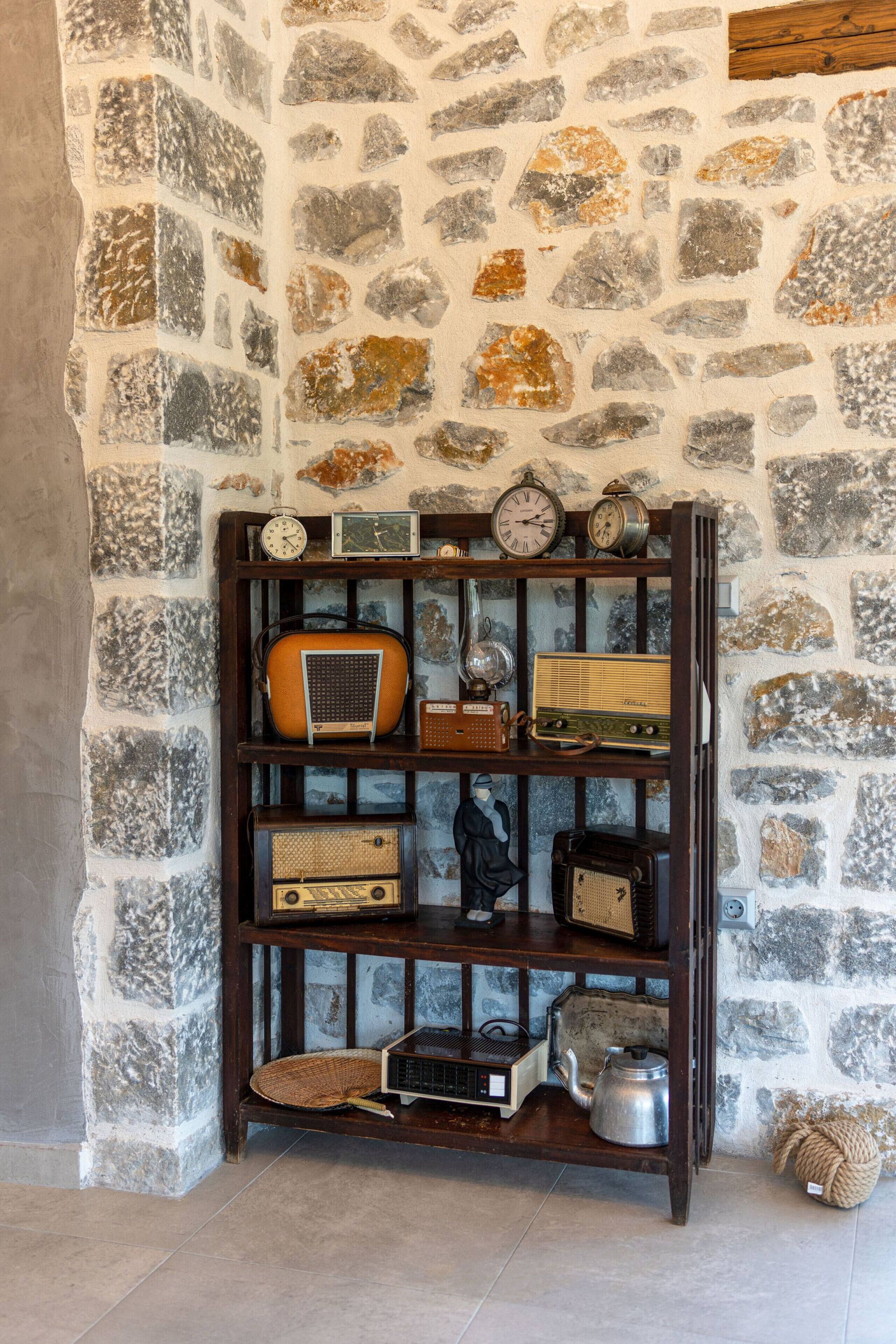 Un mur en pierre sur lequel est fixée une étagère en bois, où sont exposées de vieilles radios et une bouilloire.