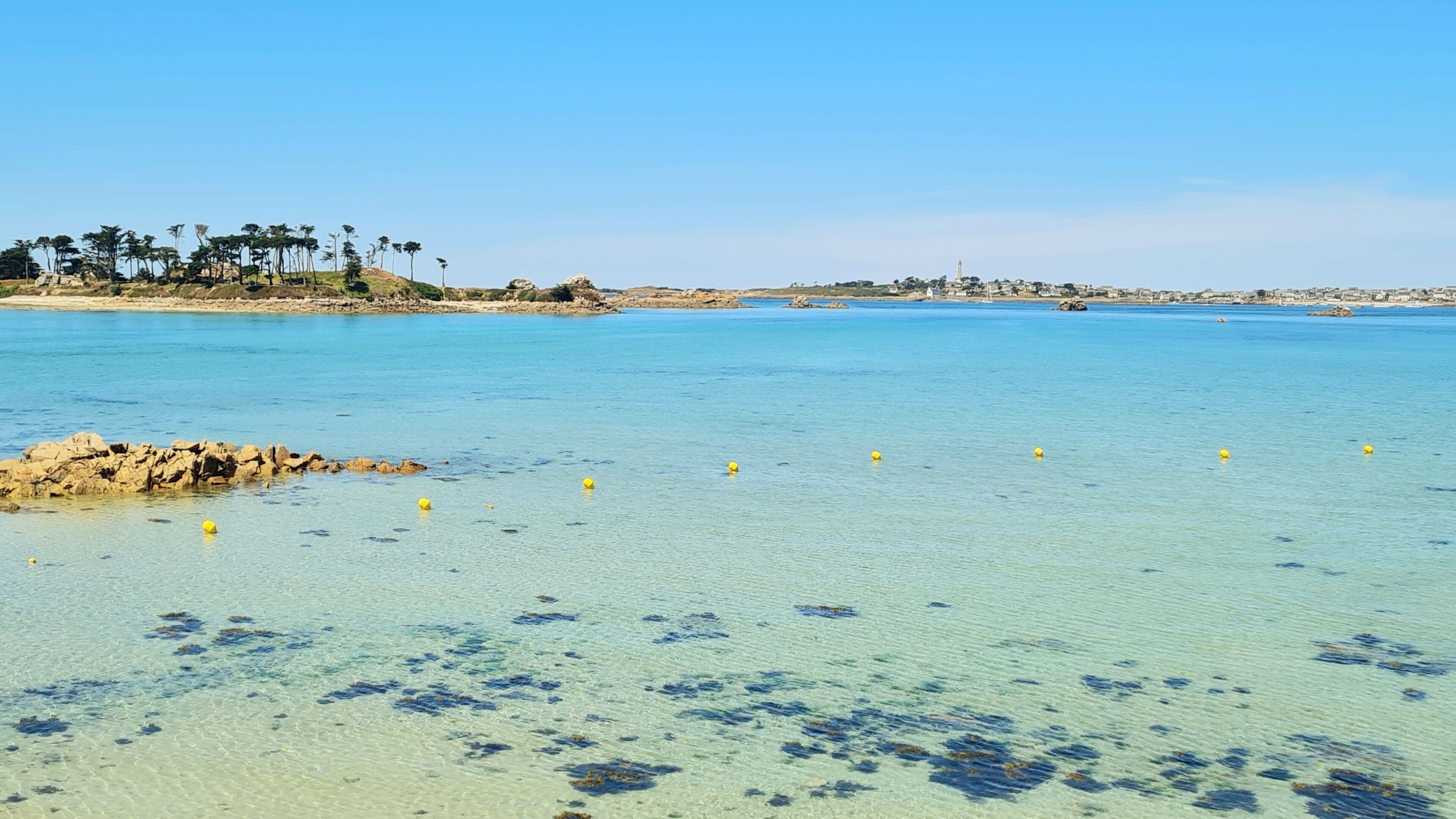 A coastal landscape with clear water, rocks, and a distant shoreline with buildings.