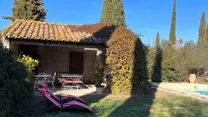 Una casa con techo de tejas, un patio con mobiliario exterior y una piscina.