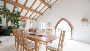 Un comedor con mesa y sillas de madera, una planta grande en maceta y vistas a través de un arco.