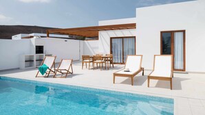 Area piscina esterna moderna con sedie a sdraio e un tavolo da pranzo, circondata da un edificio bianco con ampie finestre.