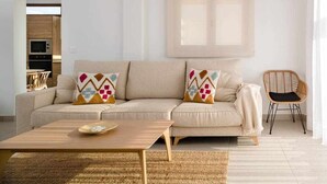 Un soggiorno moderno con un divano beige, cuscini geometrici colorati, un tavolino in legno e una sedia in vimini.