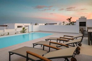 Área de piscina no terraço com espreguiçadeiras e vista desimpedida do pôr do sol.