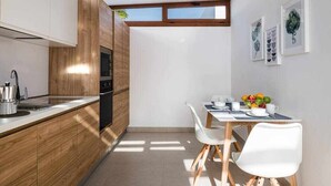 Een moderne keuken met houten kastjes, een inbouwoven en een eethoek met een witte tafel en stoelen.