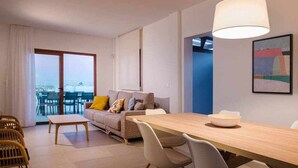 Een moderne woonkamer met een bank, eettafel en stoelen. Er is een groot raam en een deur naar een balkon.