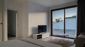 Une chambre d’hôtel moderne, équipée d’un lit, d’un téléviseur posé sur un meuble, d’une petite table ronde et offrant une vue sur la mer grâce à de grandes fenêtres.