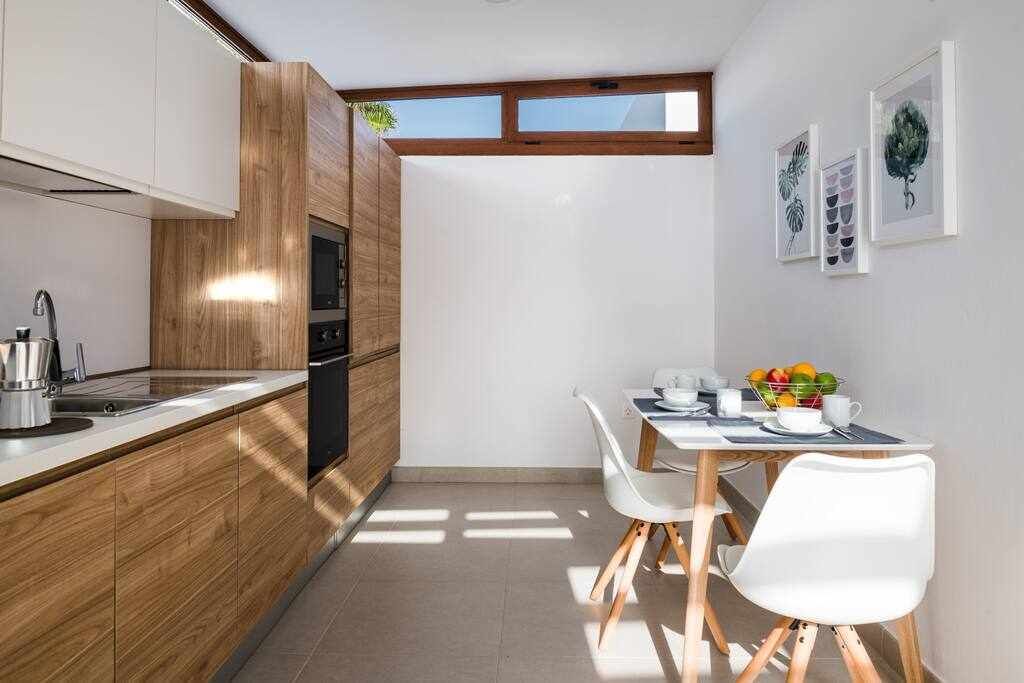 A modern kitchen with wooden cabinetry, a built-in oven, and a dining area with a white table and chairs.