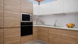 Une cuisine moderne avec des meubles de rangement en bois, un four encastré, un évier et un panier à fruits posé sur le plan de travail.