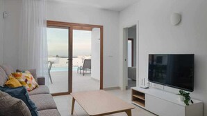 A modern living room with a sofa, a coffee table, a TV on a white stand, and a sliding glass door leading to a balcony. - Villa Zaloa, con Piscina Privada (Playa Blanca (Yaiza))
